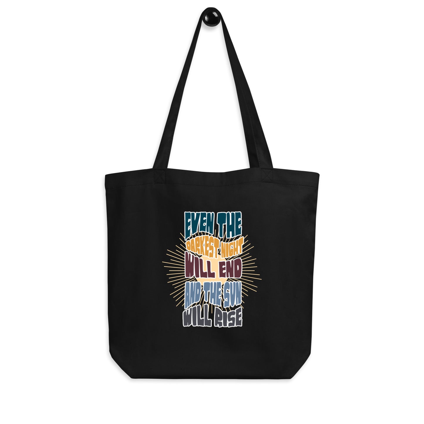A black canvas tote bag featuring an inspirational quote in colorful, stylized typography with radiating yellow lines in the background. The text reads "EVEN THE DARKEST NIGHT WILL END AND THE SUN WILL RISE" with each phrase in a different color - blue, orange, purple, and light blue respectively. The bag has two black shoulder straps and a spacious rectangular shape.