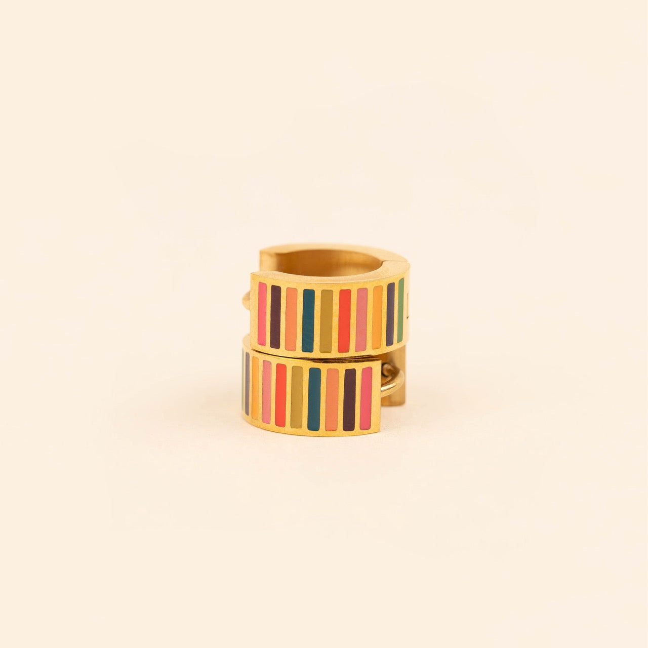 Pair of small gold-plated stainless steel hoop earrings with colorful horizontal stripes in pink, burgundy, orange, teal, and red enamel, photographed on a beige background