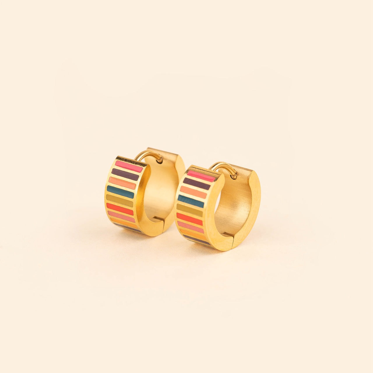 Pair of small gold-plated stainless steel hoop earrings with colorful horizontal stripes in pink, burgundy, orange, teal, and red enamel, photographed on a beige background