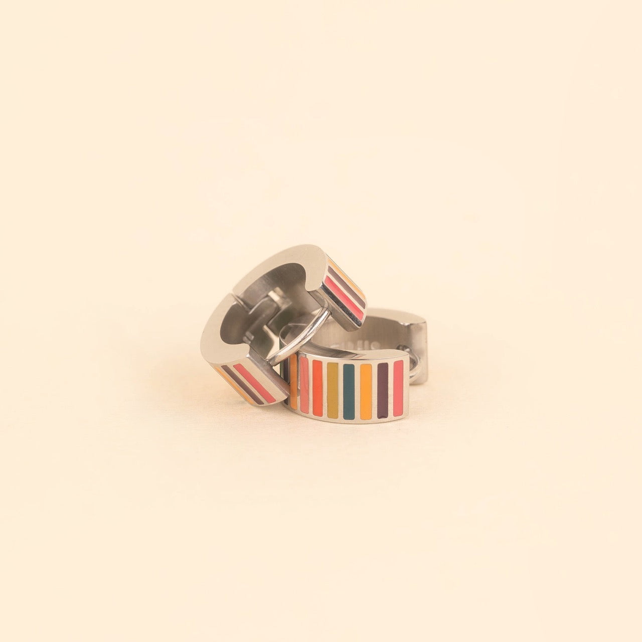 Pair of small gold-plated stainless steel hoop earrings with colorful horizontal stripes in pink, burgundy, orange, teal, and red enamel, photographed on a beige background