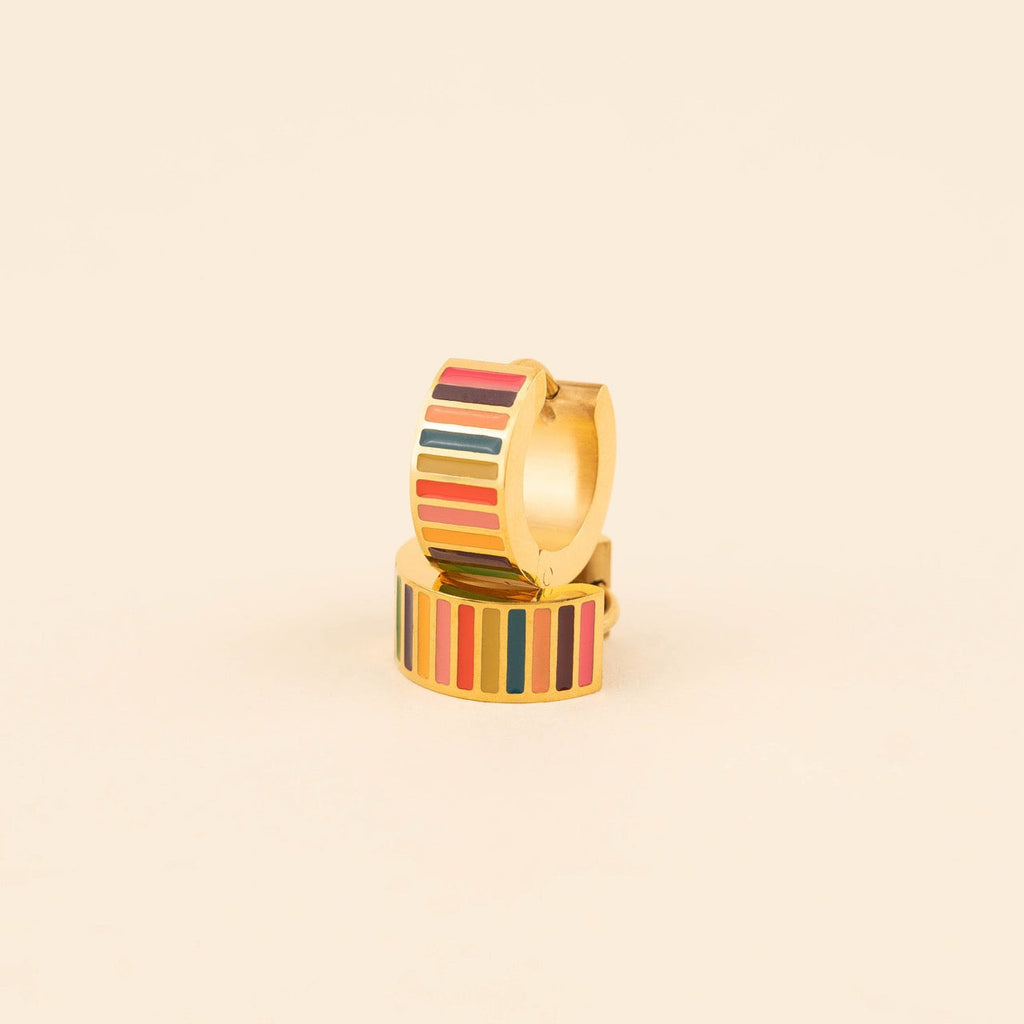 Pair of small gold-plated stainless steel hoop earrings with colorful horizontal stripes in pink, burgundy, orange, teal, and red enamel, photographed on a beige background