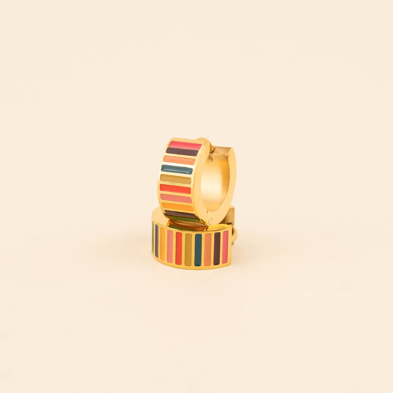 Pair of small gold-plated stainless steel hoop earrings with colorful horizontal stripes in pink, burgundy, orange, teal, and red enamel, photographed on a beige background