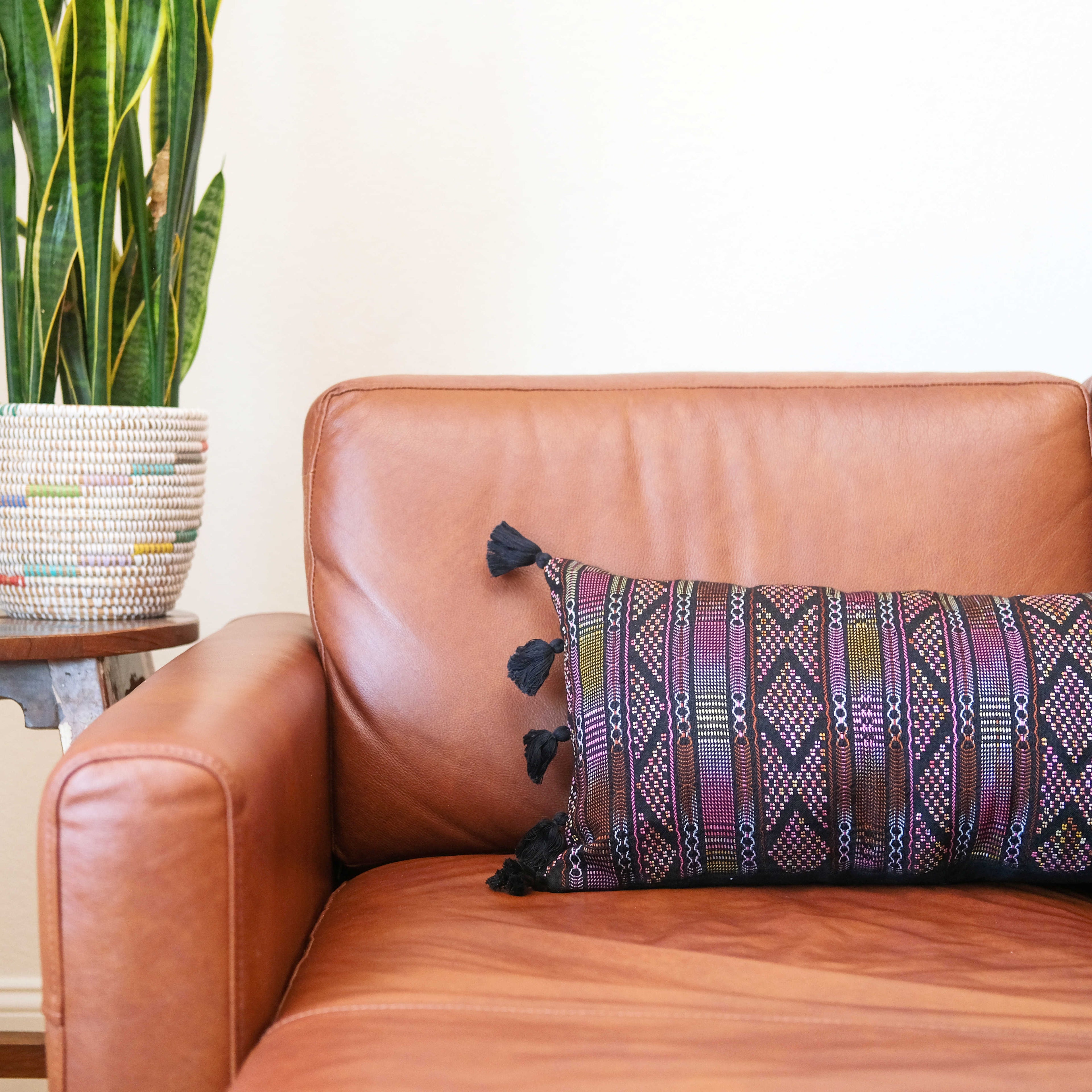 Hand woven lumbar pillow from Guatemala featuring intricate geometric patterns in vibrant colors including black, blue, and pink on a dark background, with black tassel trim along both long edges, displayed against a white background