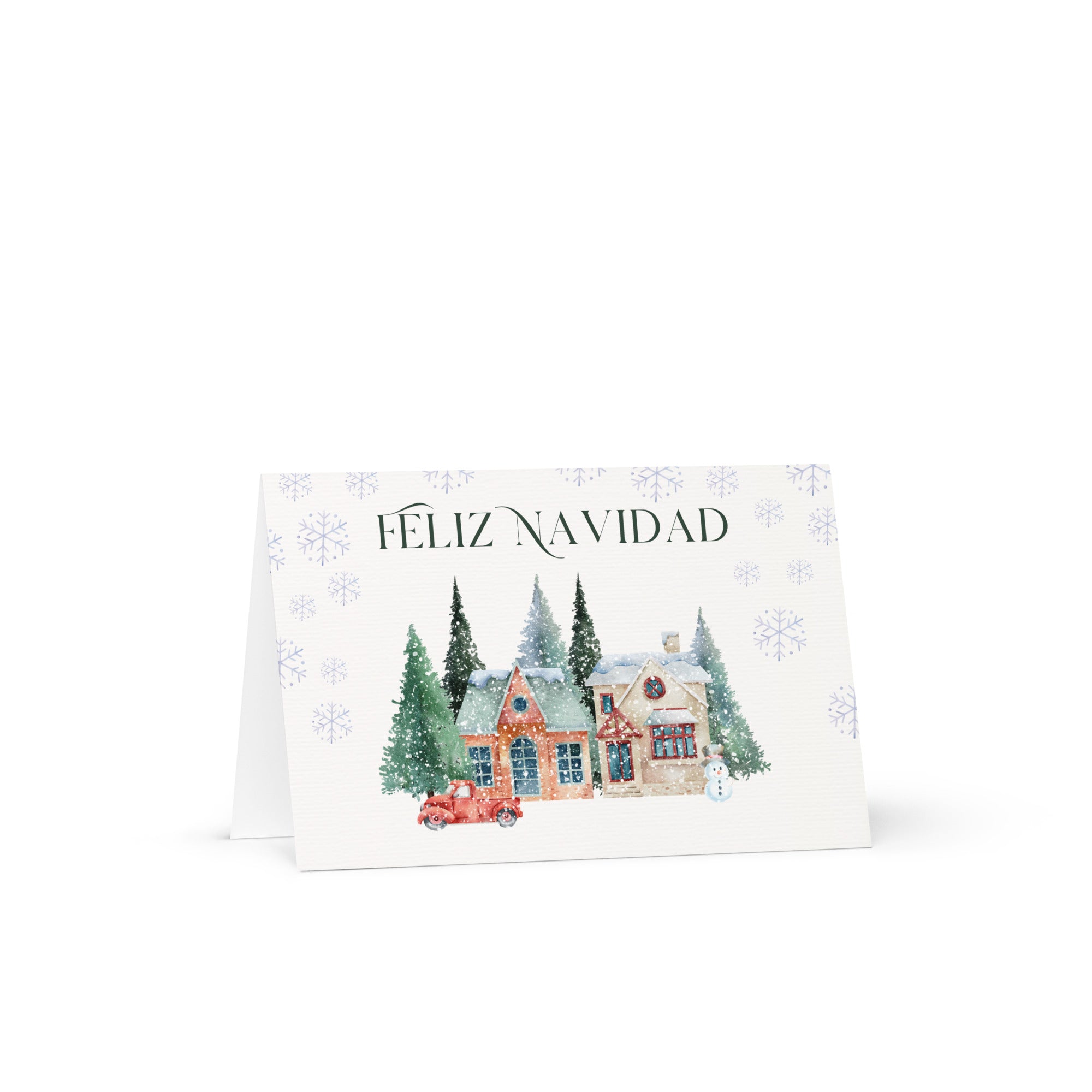 Spanish Christmas greeting card featuring "Feliz Navidad" text with watercolor illustration of snowy village scene with cottages, pine trees, snowman, and vintage truck surrounded by delicate snowflake pattern, displayed with white envelope