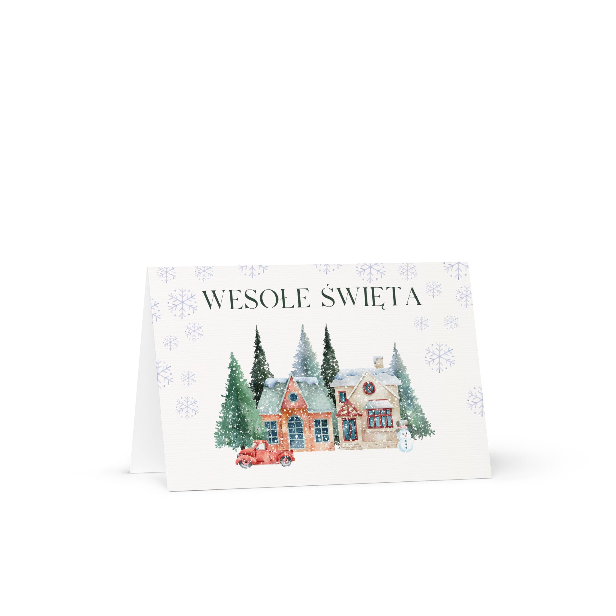 Polish Christmas greeting card featuring "Wesołe Święta" text with watercolor illustration of snowy village scene with cottages, pine trees, snowman, and vintage truck surrounded by delicate snowflake pattern, displayed with white envelope
