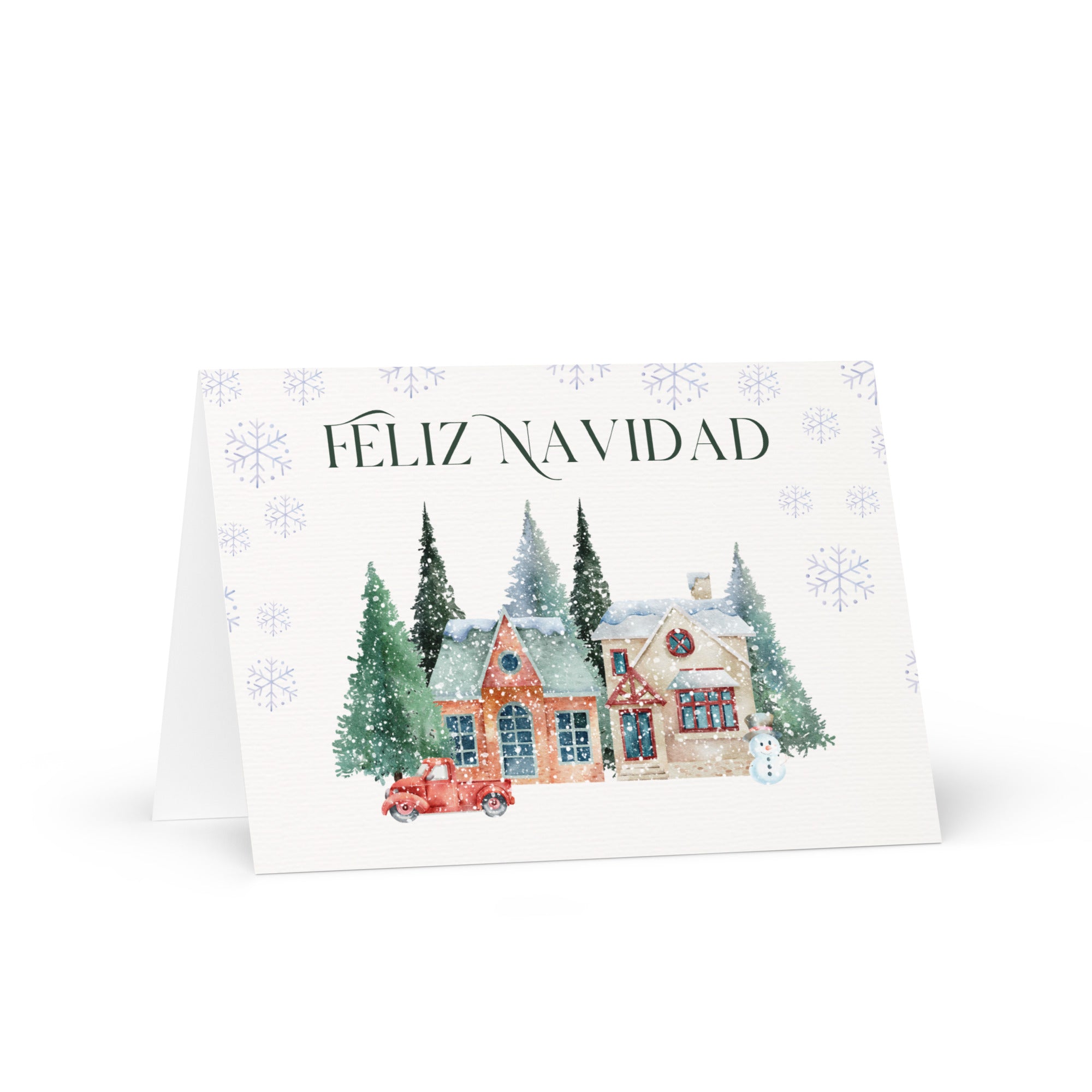 Spanish Christmas greeting card featuring "Feliz Navidad" text with watercolor illustration of snowy village scene with cottages, pine trees, snowman, and vintage truck surrounded by delicate snowflake pattern, displayed with white envelope