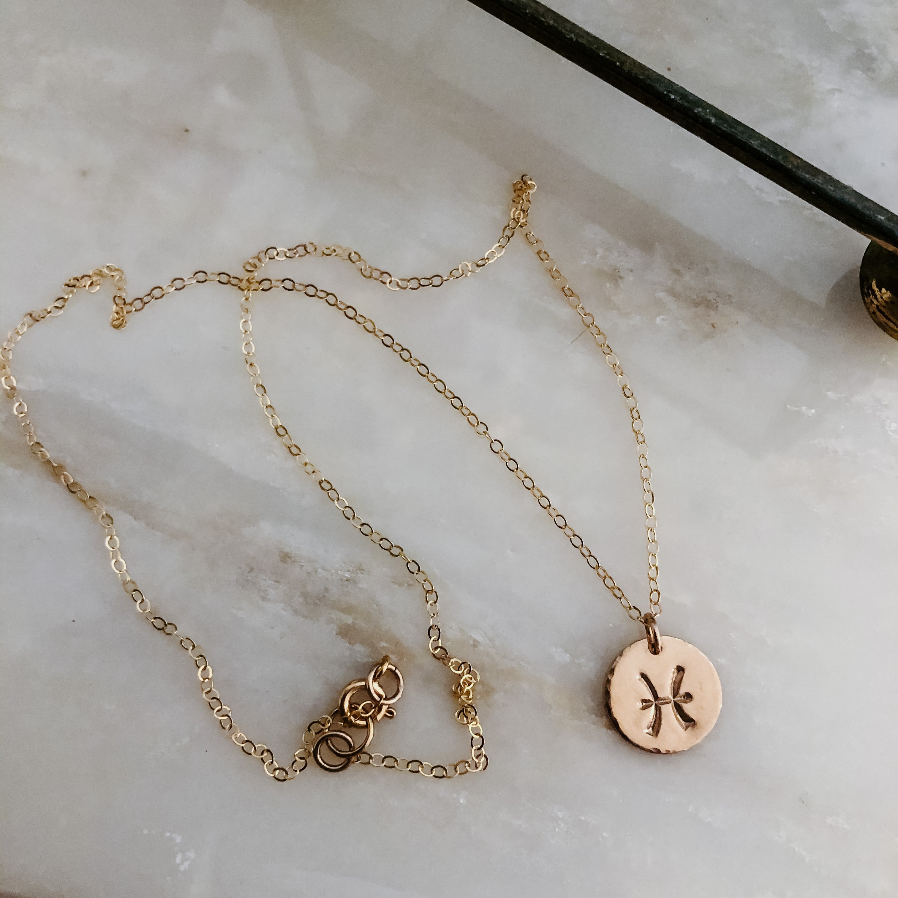 Collection of hand-stamped zodiac sign necklaces in gold and silver featuring circular pendants with astrological symbols including Aquarius, Scorpio, Taurus, Sagittarius, Cancer, Leo, Aries, Gemini, and Libra, displayed with delicate chains on a marble surface