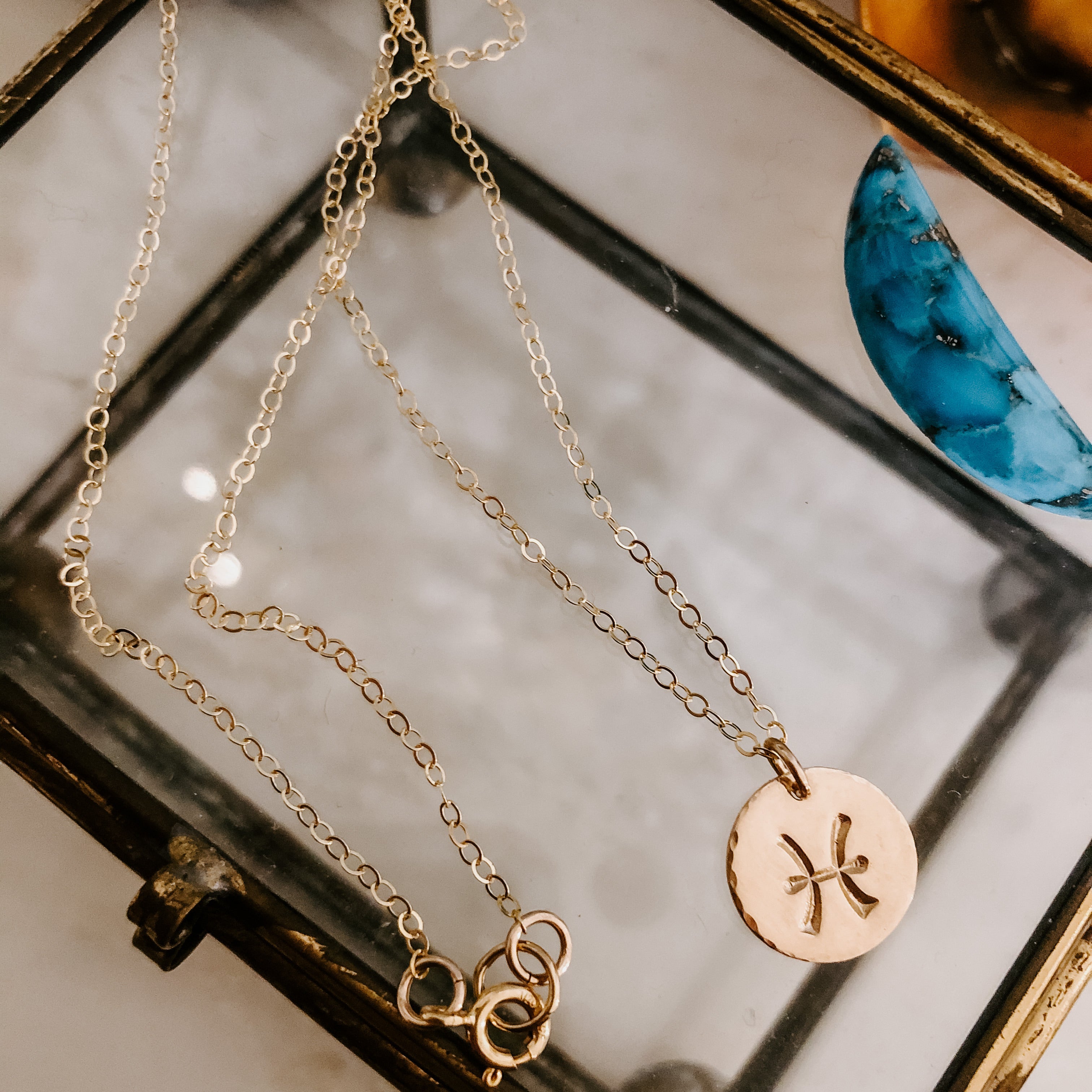 Collection of hand-stamped zodiac sign necklaces in gold and silver featuring circular pendants with astrological symbols including Aquarius, Scorpio, Taurus, Sagittarius, Cancer, Leo, Aries, Gemini, and Libra, displayed with delicate chains on a marble surface