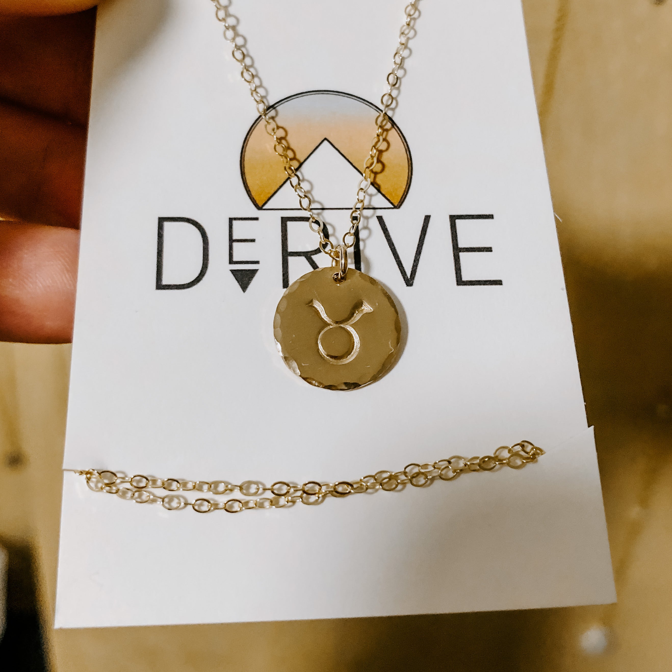 Collection of hand-stamped zodiac sign necklaces in gold and silver featuring circular pendants with astrological symbols including Aquarius, Scorpio, Taurus, Sagittarius, Cancer, Leo, Aries, Gemini, and Libra, displayed with delicate chains on a marble surface