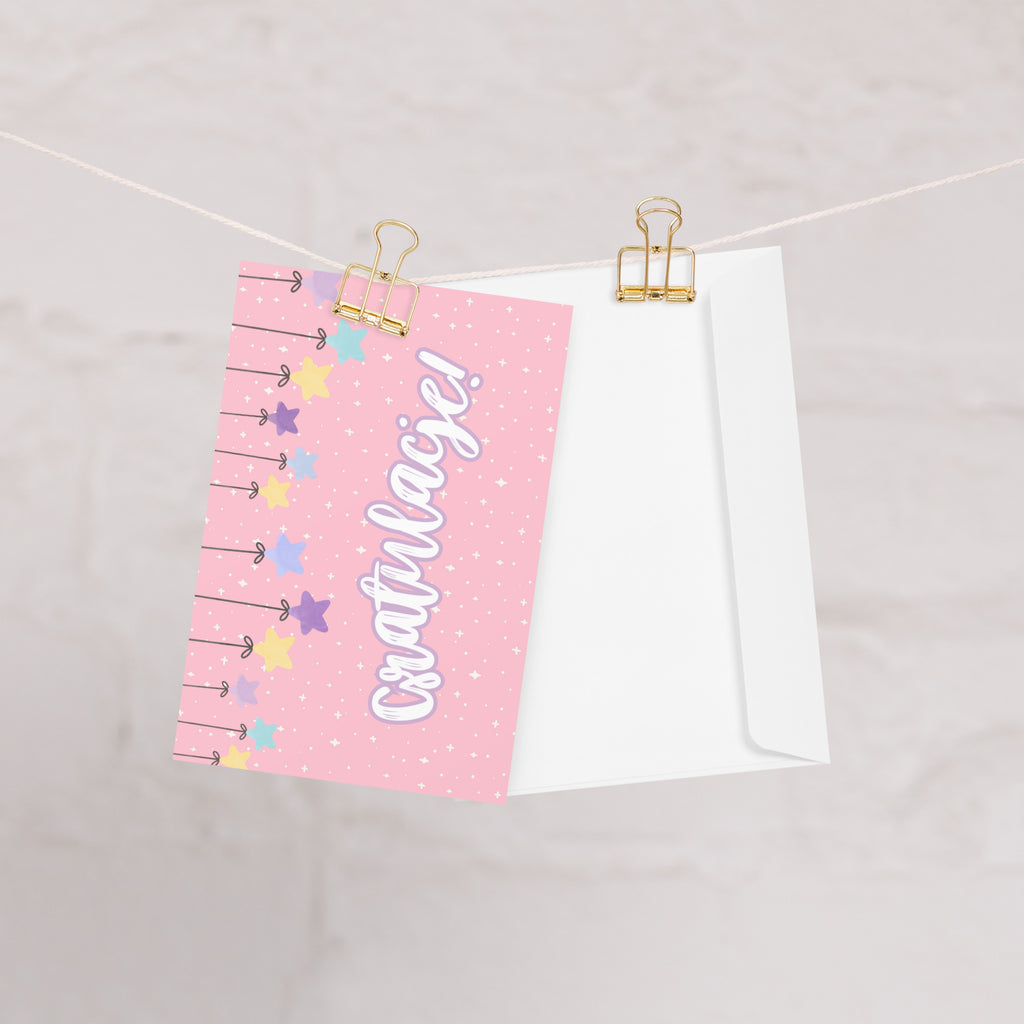 Polish greeting card with pink background featuring "Gratulacje!" text in white script lettering, decorated with hanging colorful stars and small sparkle details throughout