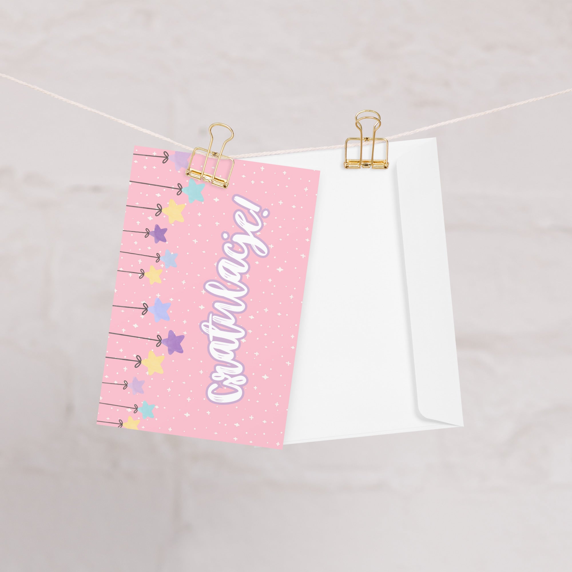 Polish greeting card with pink background featuring "Gratulacje!" text in white script lettering, decorated with hanging colorful stars and small sparkle details throughout