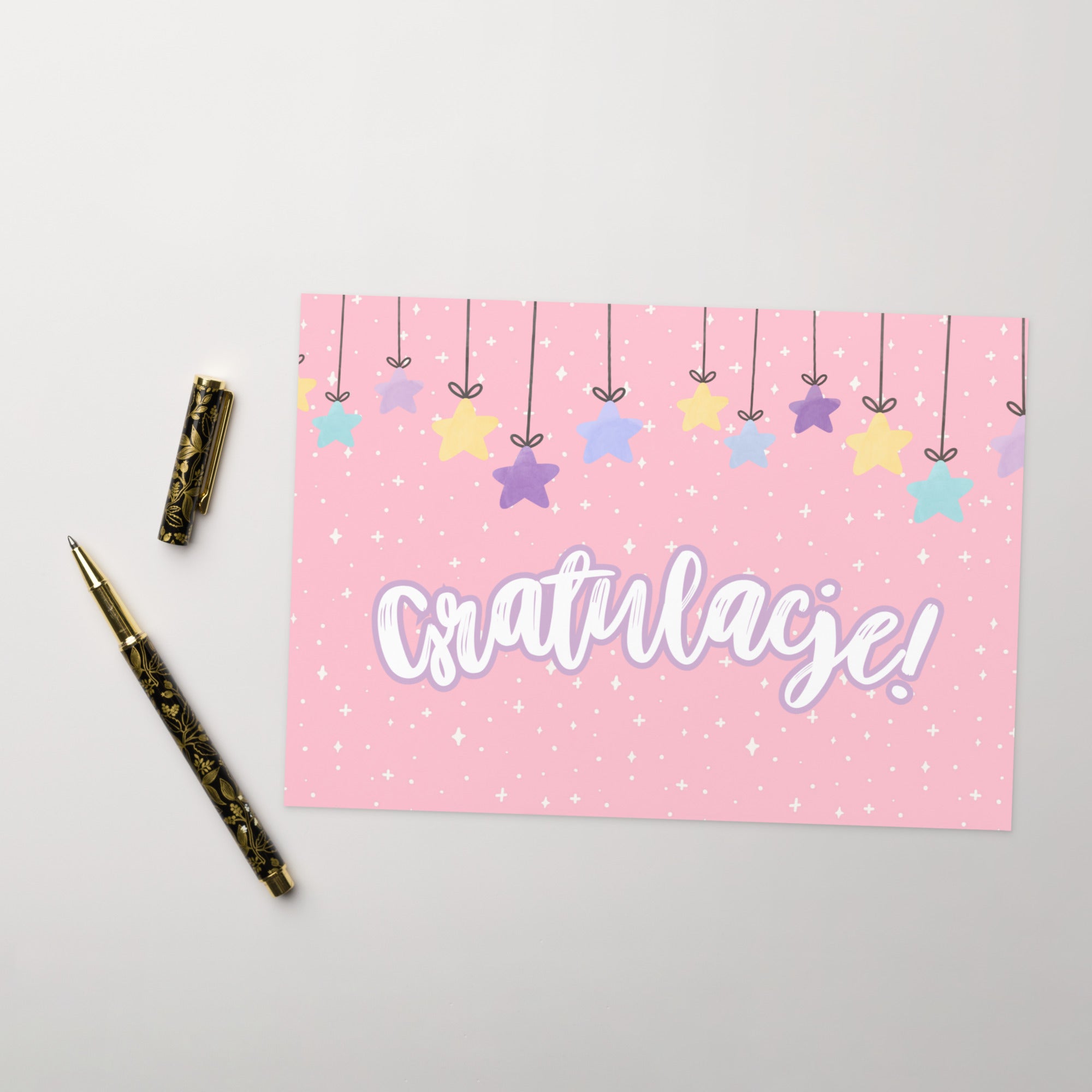 Polish greeting card with pink background featuring "Gratulacje!" text in white script lettering, decorated with hanging colorful stars and small sparkle details throughout