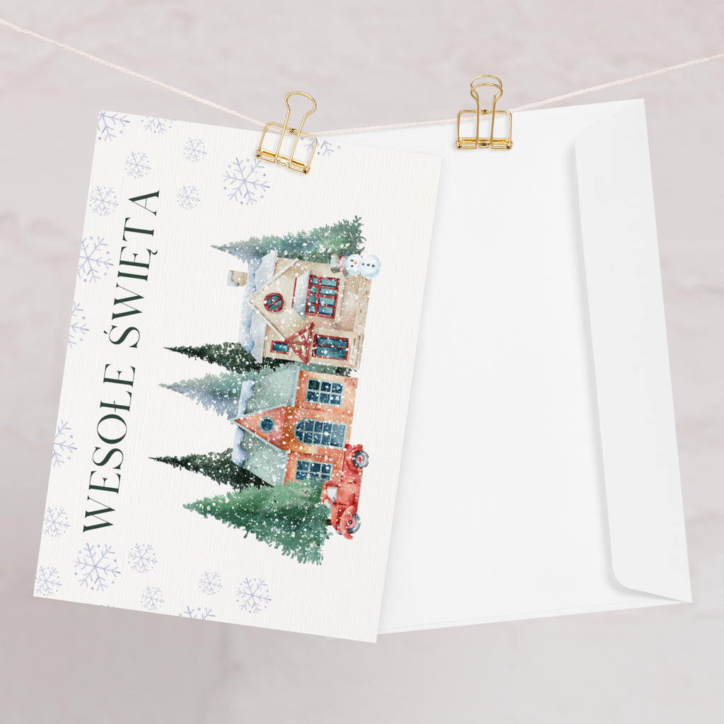 Polish Christmas greeting card featuring "Wesołe Święta" text with watercolor illustration of snowy village scene with cottages, pine trees, snowman, and vintage truck surrounded by delicate snowflake pattern, displayed with white envelope
