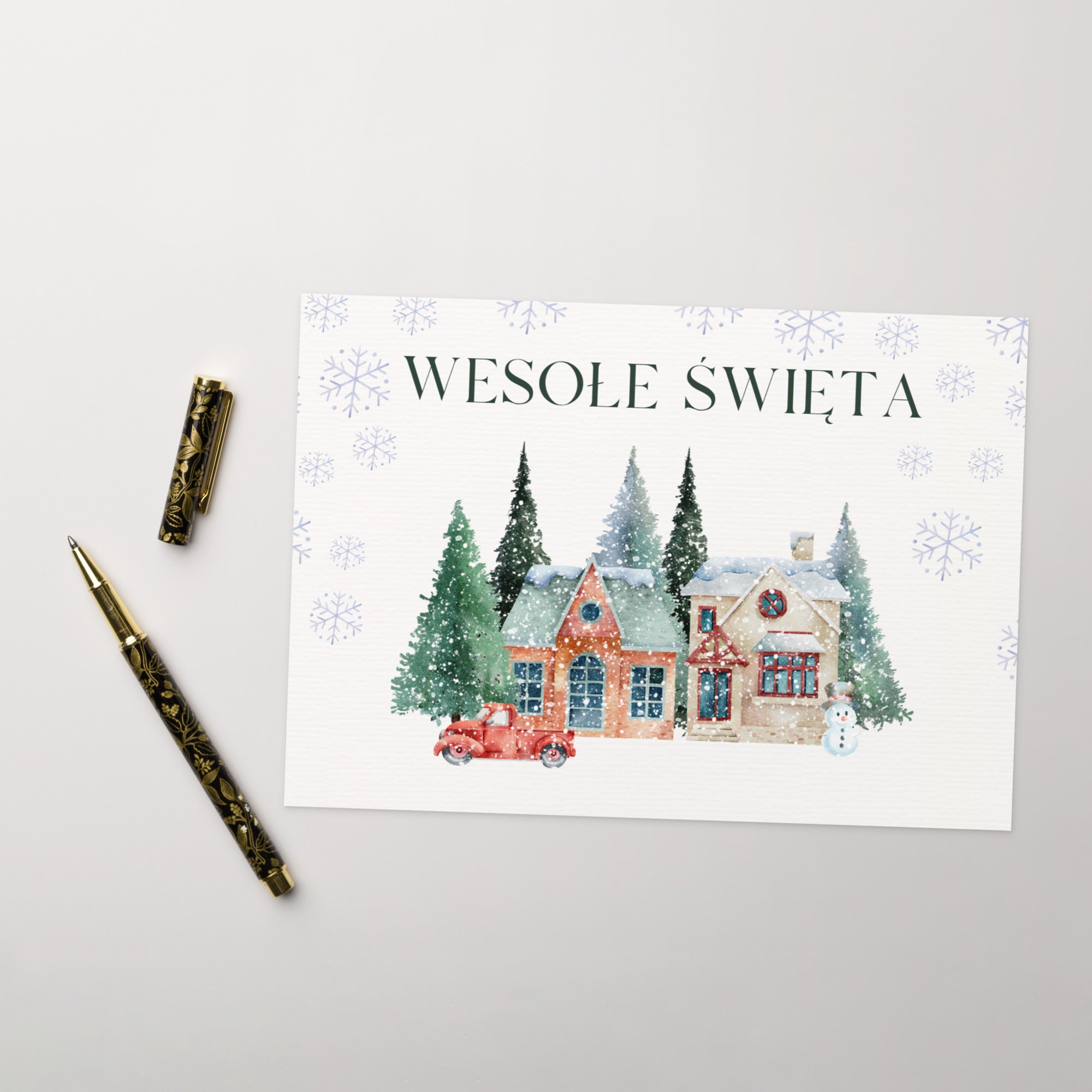 Polish Christmas greeting card featuring "Wesołe Święta" text with watercolor illustration of snowy village scene with cottages, pine trees, snowman, and vintage truck surrounded by delicate snowflake pattern, displayed with white envelope