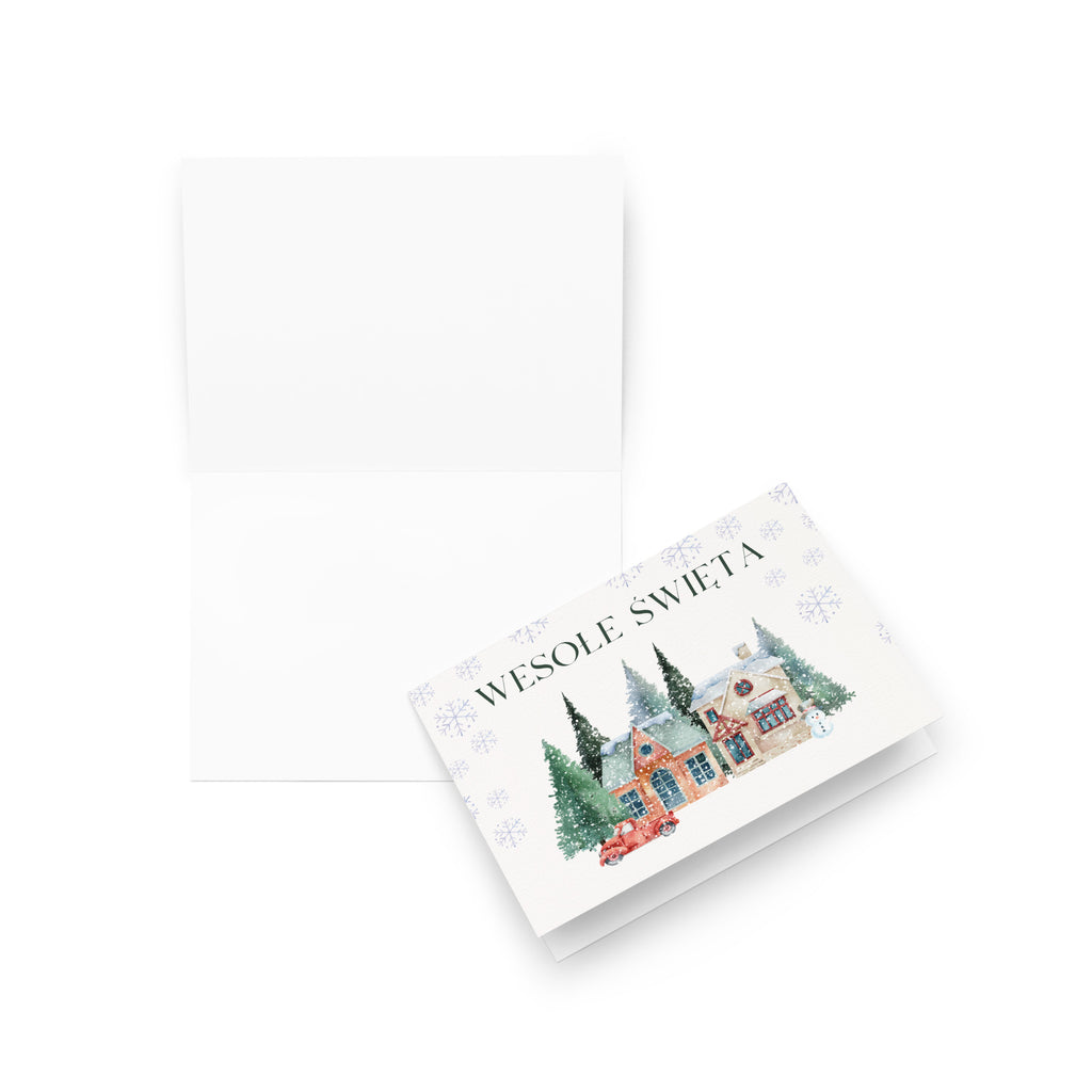 Polish Christmas greeting card featuring "Wesołe Święta" text with watercolor illustration of snowy village scene with cottages, pine trees, snowman, and vintage truck surrounded by delicate snowflake pattern, displayed with white envelope