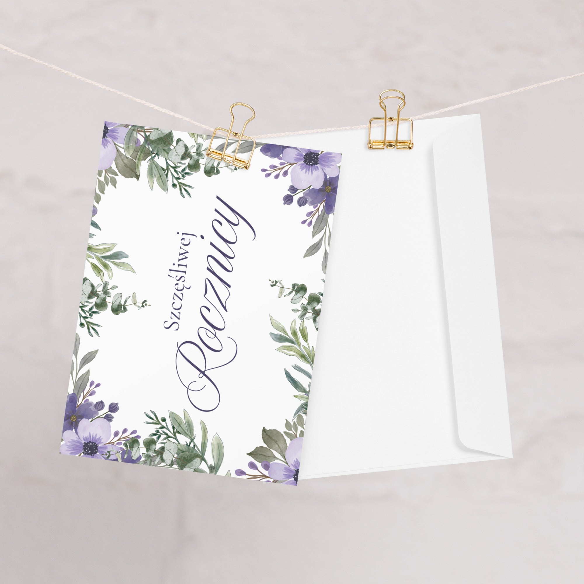 Polish anniversary greeting card featuring "szczęśliwej rocznicy" text in elegant script on white background, decorated with watercolor purple flowers and green botanical leaves in corner arrangement