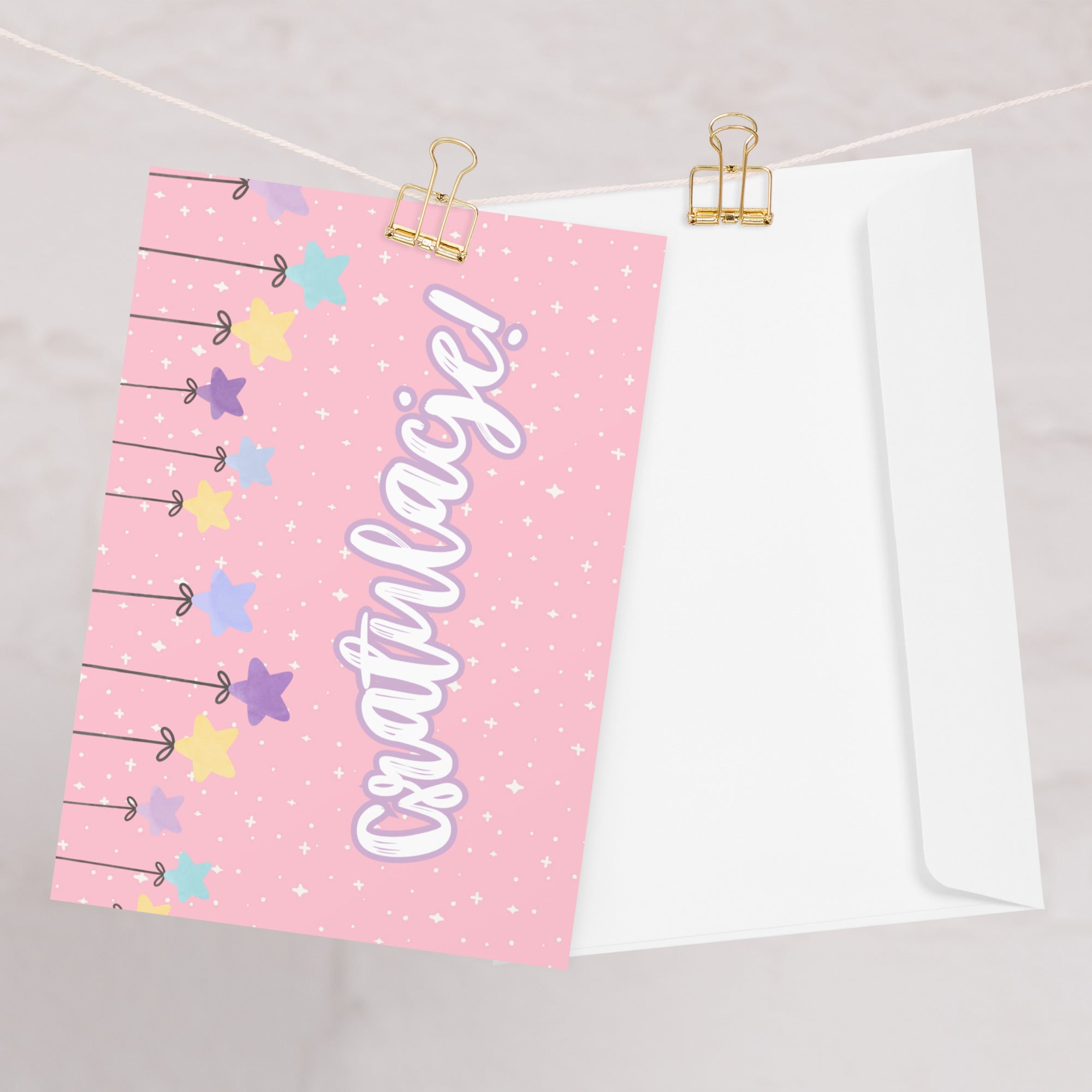 Polish greeting card with pink background featuring "Gratulacje!" text in white script lettering, decorated with hanging colorful stars and small sparkle details throughout