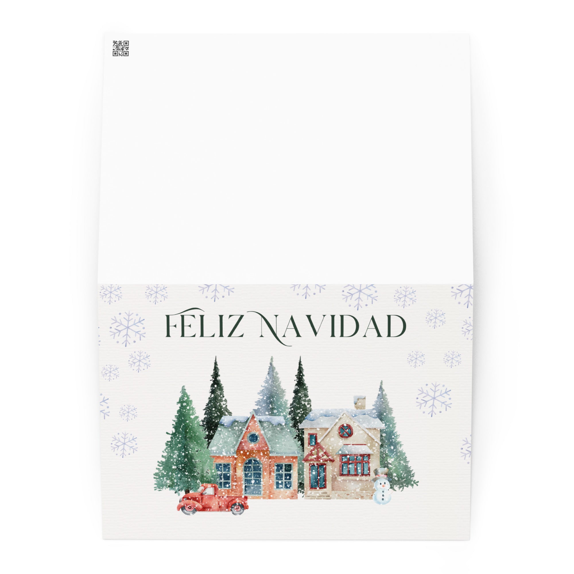 Spanish Christmas greeting card featuring "Feliz Navidad" text with watercolor illustration of snowy village scene with cottages, pine trees, snowman, and vintage truck surrounded by delicate snowflake pattern, displayed with white envelope