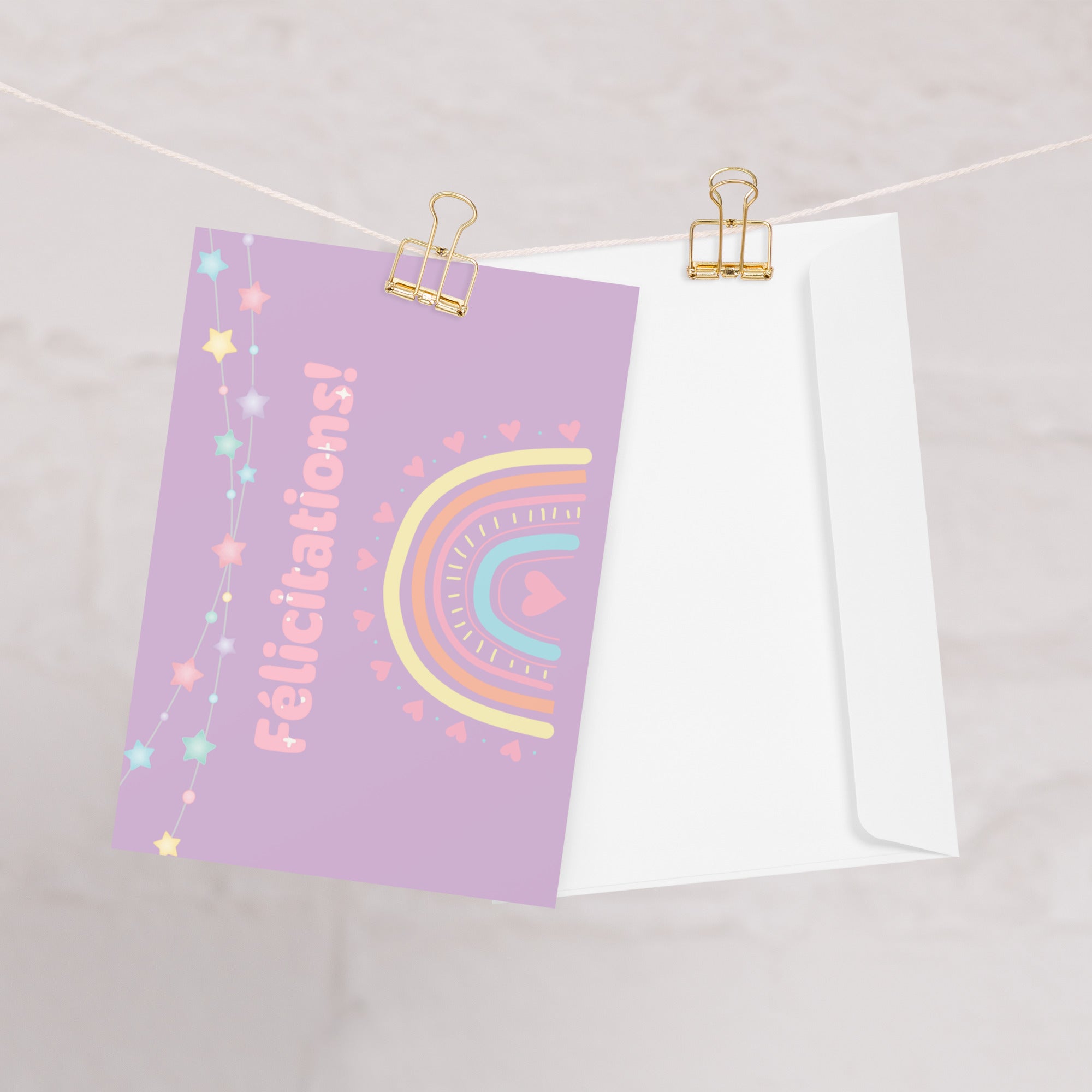 French greeting card with purple background featuring "Félicitations!" text in pink letters, decorated with a pastel rainbow, colorful star garland, and small heart details