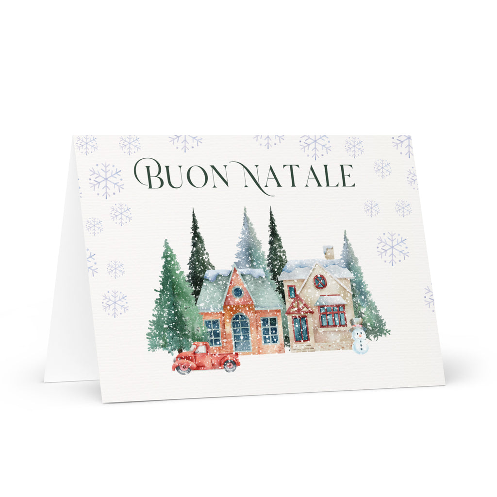 Italian Christmas greeting card featuring "Buon Natale" text with watercolor illustration of snowy village scene with cottages, pine trees, snowman, and vintage truck surrounded by delicate snowflake pattern