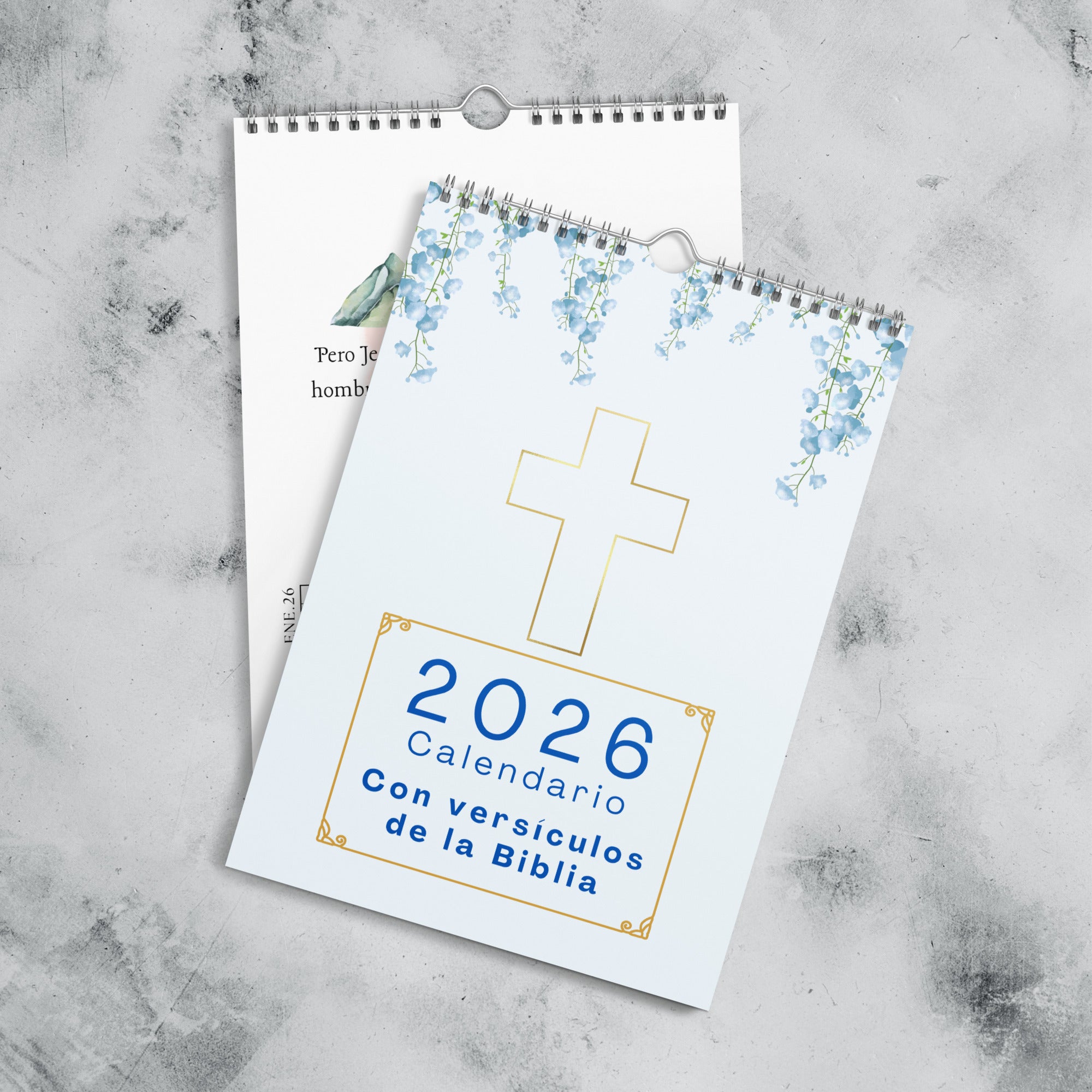2026 Spanish calendar cover featuring light blue background with watercolor blue flowers at top, gold outlined cross in center, and title text "2026 Calendario Con versículos de la Biblia" in blue lettering within decorative gold frame