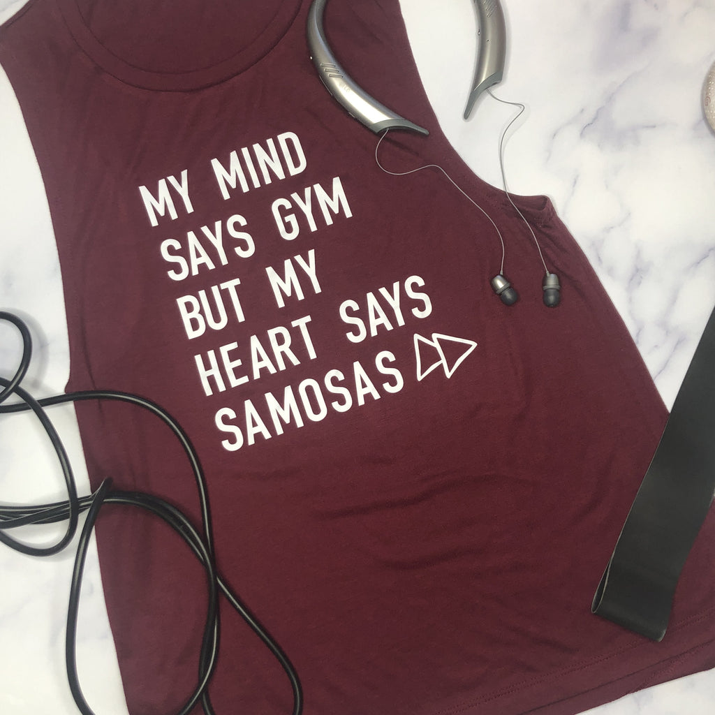 Maroon tank top with text 'My mind says gym but my heart says samosas' on a marble surface.